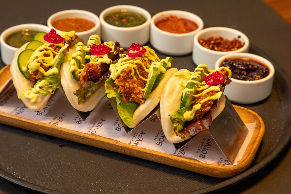 Give Taco Night a Crunchy Plot Twist With These Crispy Tofu Lettuce Wraps 1 Close-up of gourmet bao buns with chicken filling and a variety of dipping sauces in bowls.