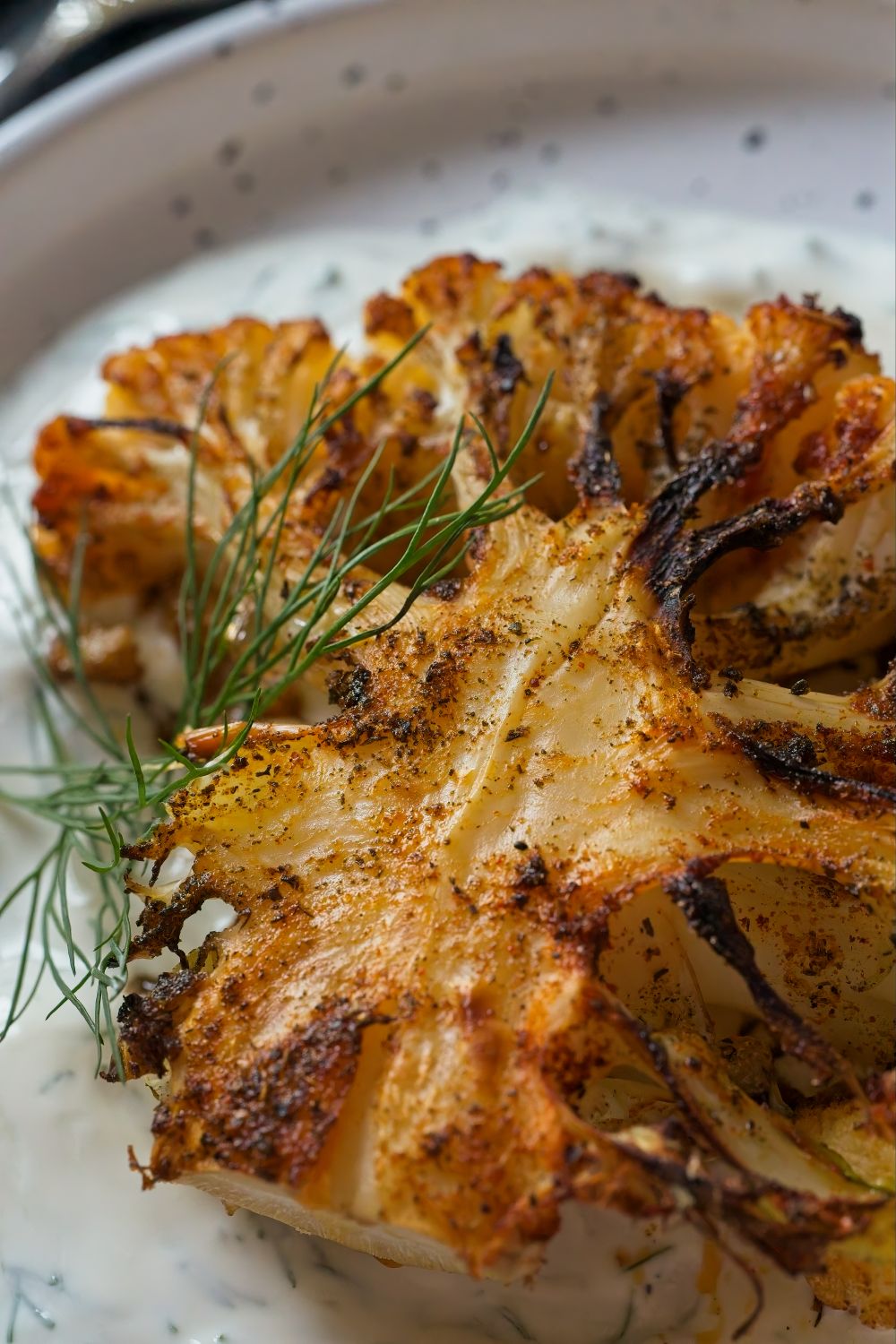 Give Cauliflower the Steak Treatment And Watch It Steal the Dinner Show 2 Close-up of grilled cauliflower seasoned with dill on a white plate.