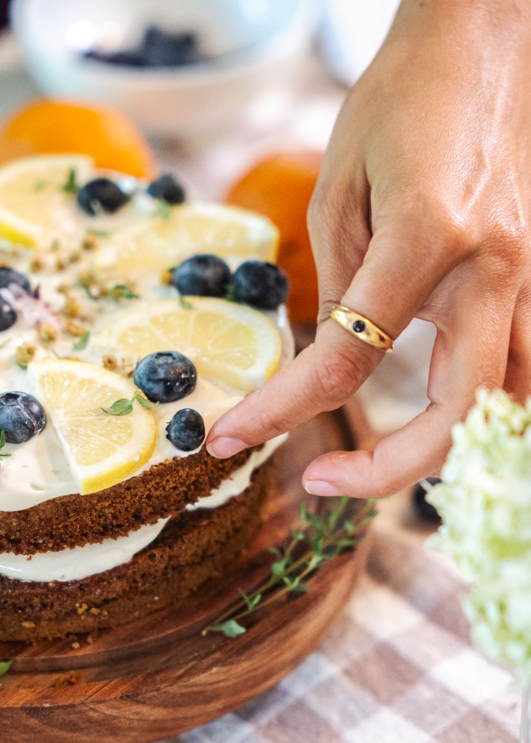 Close-up of hand decorating a lemon blueberry cake with fruit slices and berries on a wooden board.