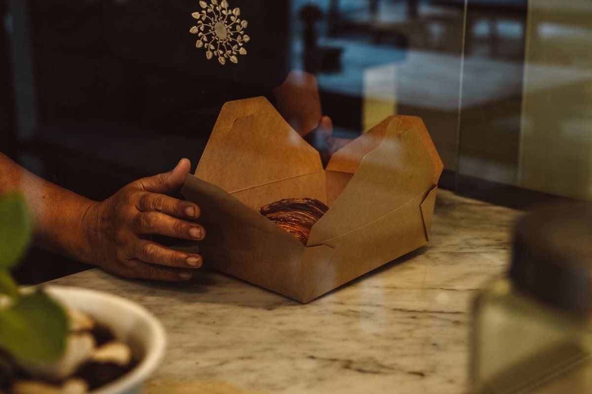 5 Small Food Container Details With Surprisingly Useful Jobs 1 Close-up of hands holding a takeaway box with bread on a marble counter.
