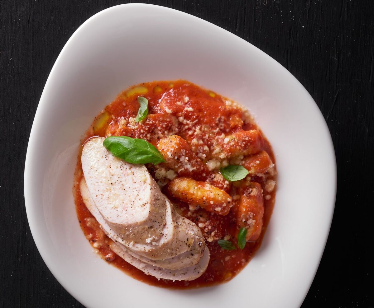 Close-up of Italian gnocchi with marinara sauce, cheese, and basil leaves.