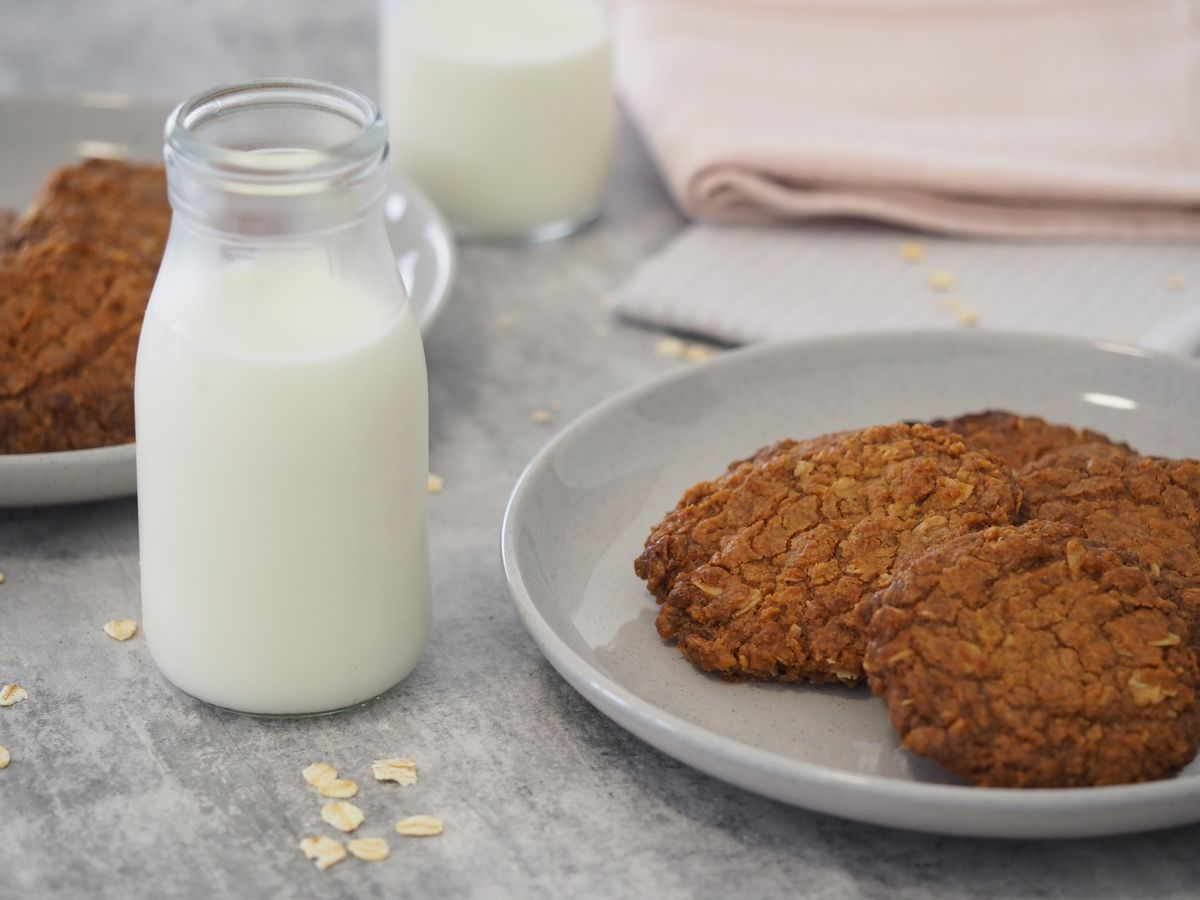 Close-up of oatmeal cookies with milk in glass bottle on a kitchen counter.