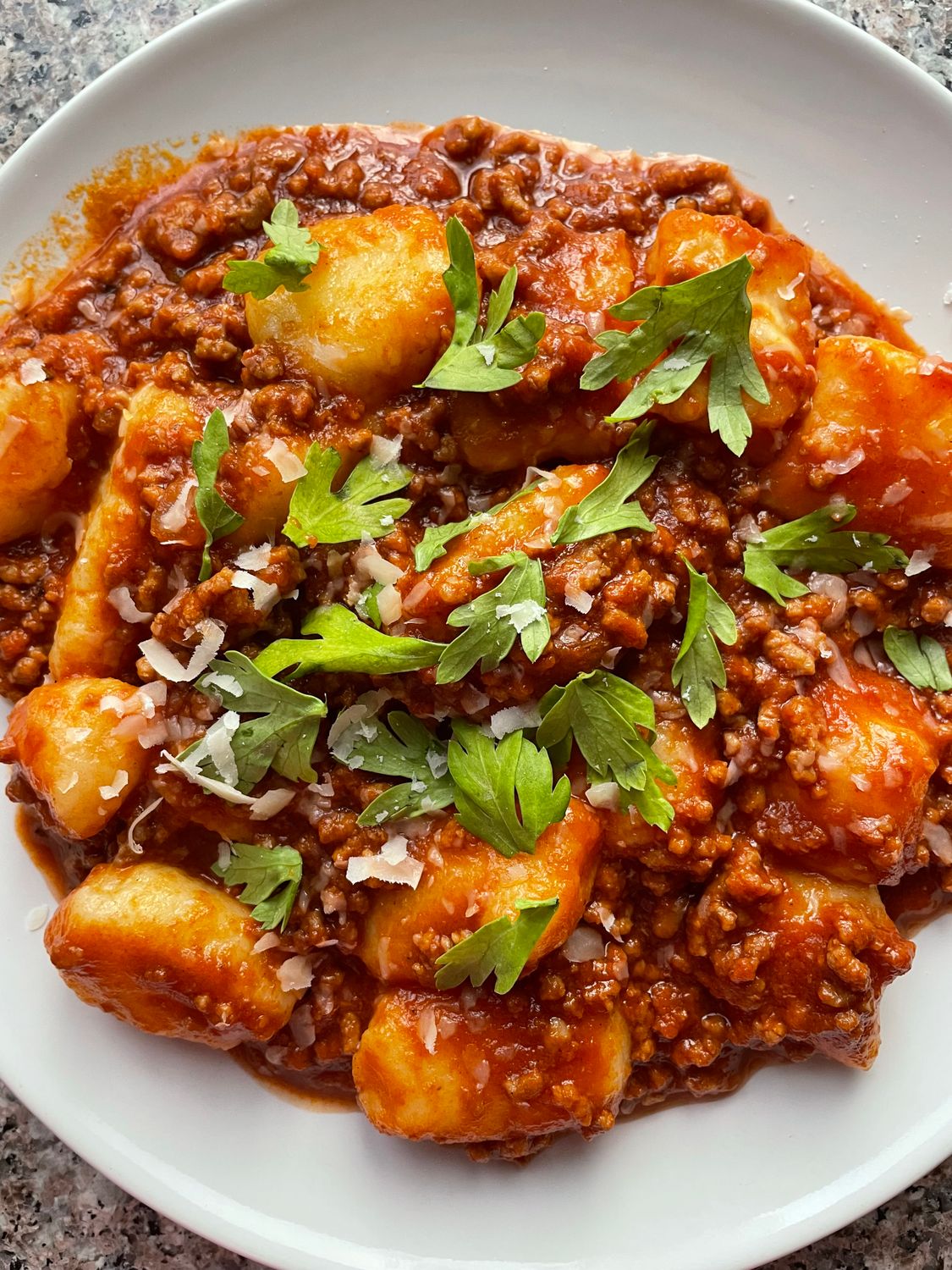 Close-up of savory gnocchi topped with rich meat sauce and garnished with herbs.