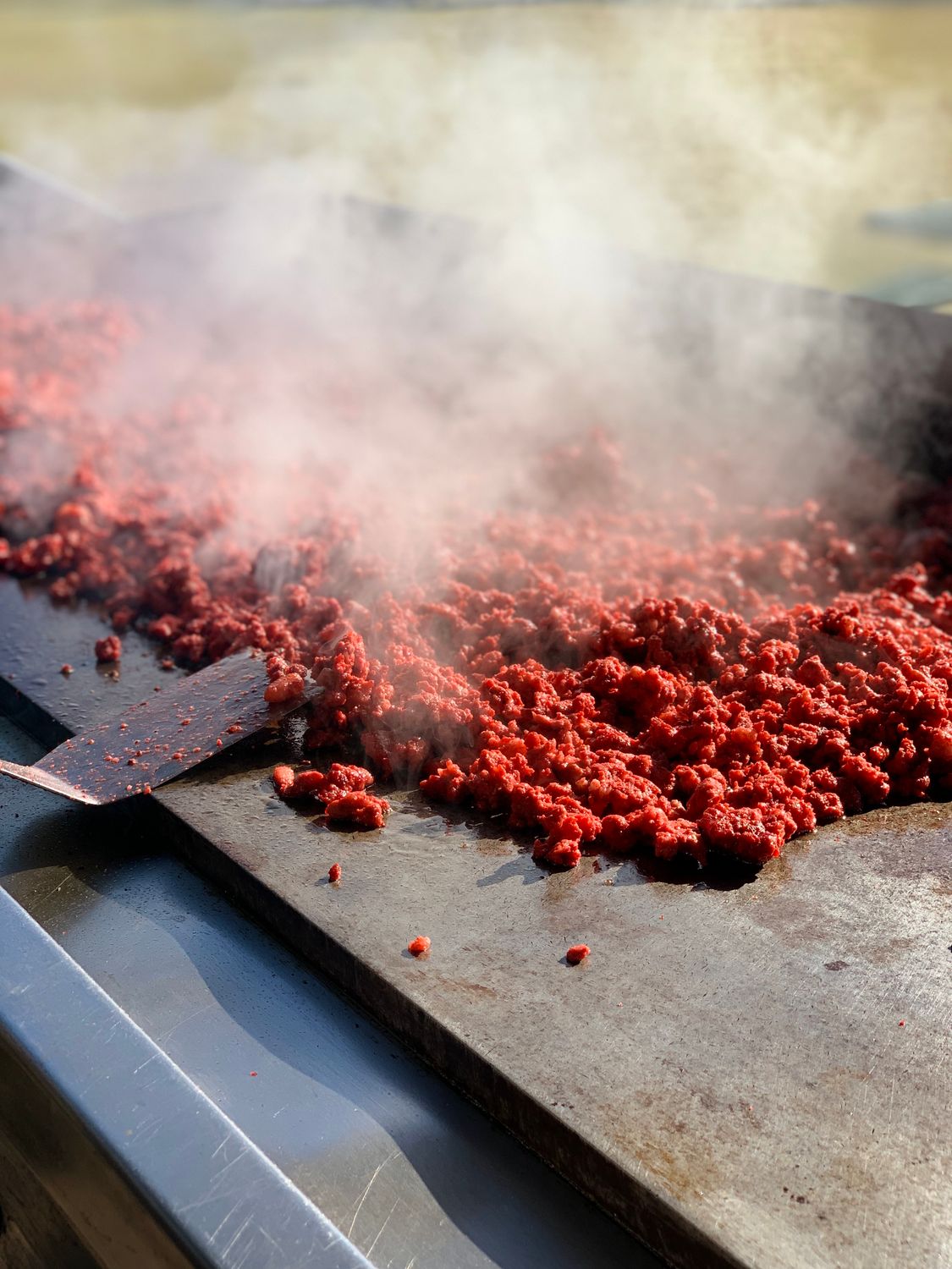 7 Foods Americans Used to Love But Can’t Afford Anymore 1 Close-up of sizzling ground beef cooking on hot grill with steam rising.