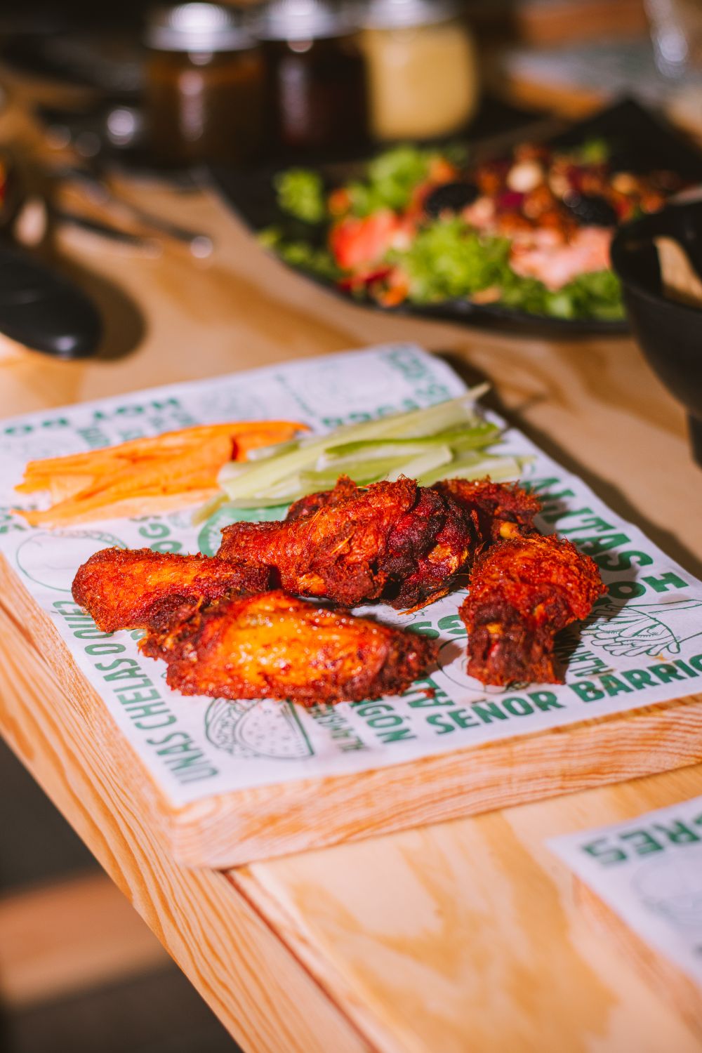 Close-up of spicy chicken wings with celery and carrots on a wooden platter.