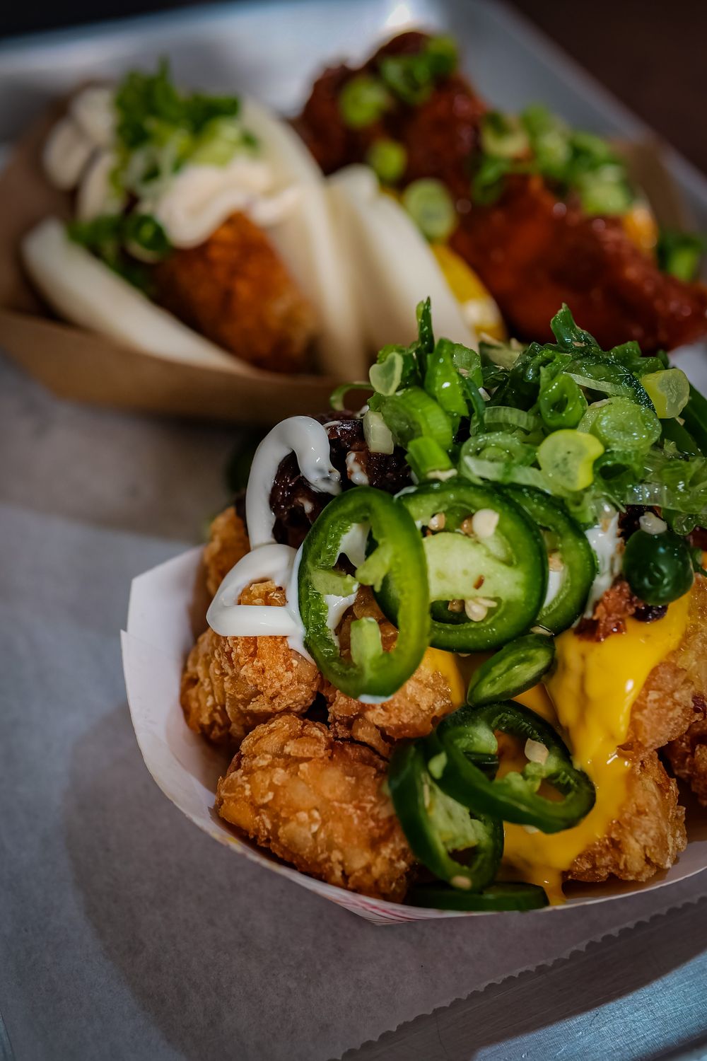 Close-up of spicy loaded tater tots topped with jalapenos and side bao buns, perfect for foodies.