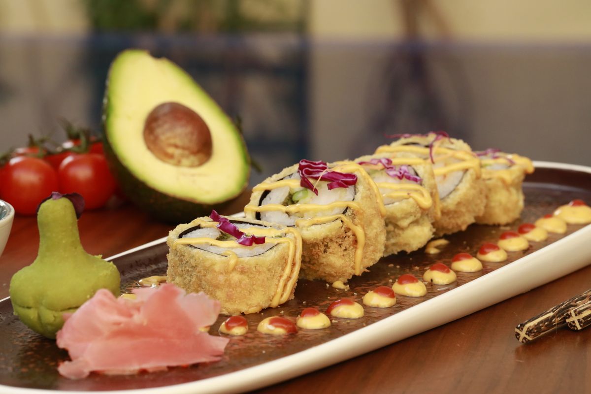 Close-up of sushi roll with avocado, wasabi, and garnish on a wooden table.