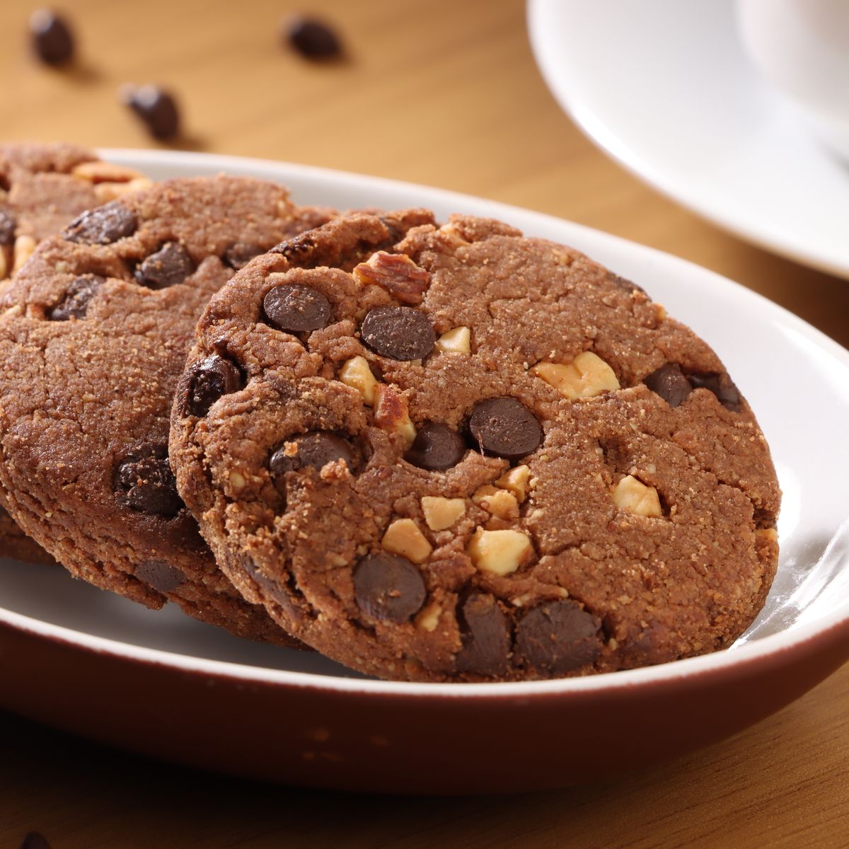 Close-up of three chocolate chip cookies with nuts on a white plate.