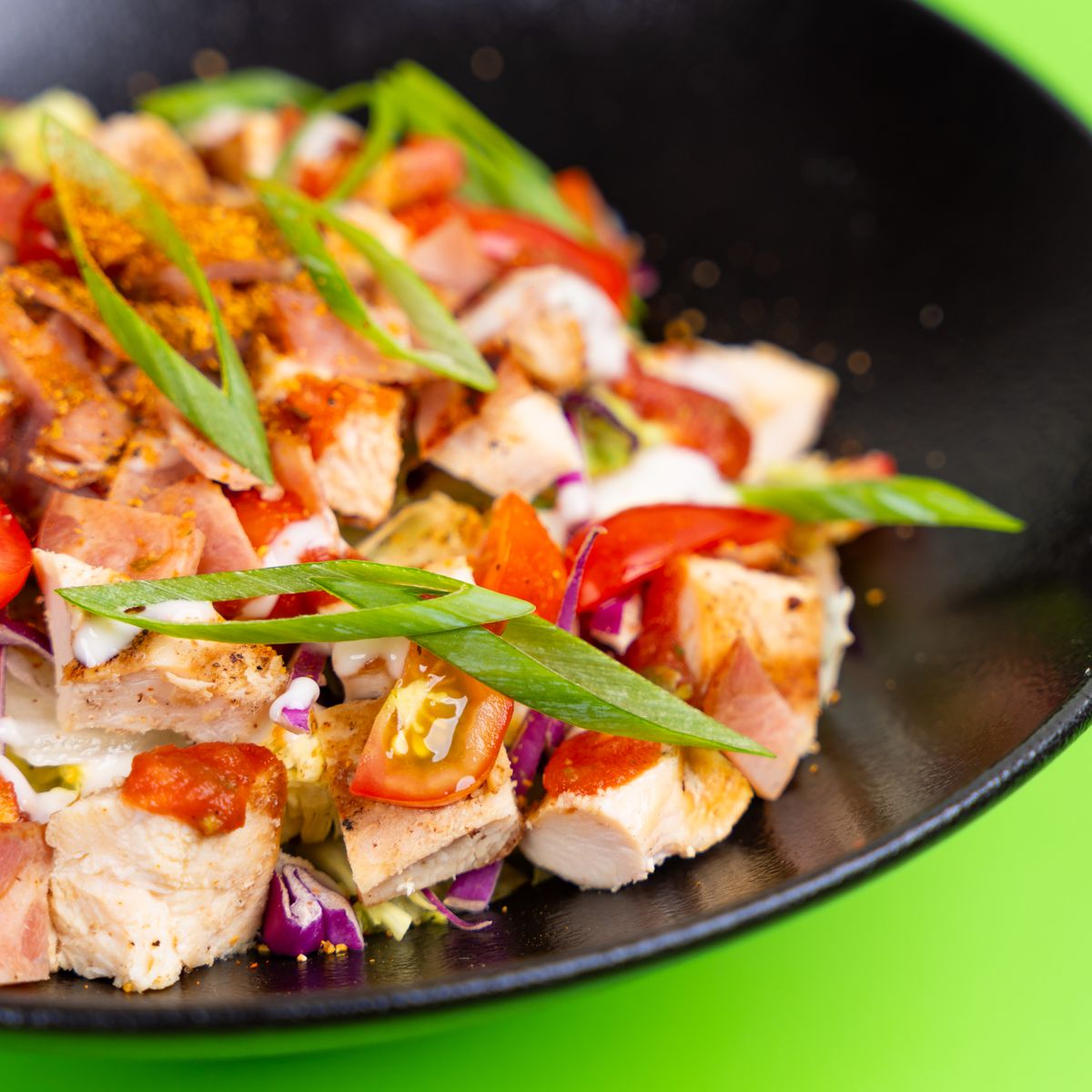 Close-up of vibrant chicken salad with fresh vegetables in a chic black bowl.