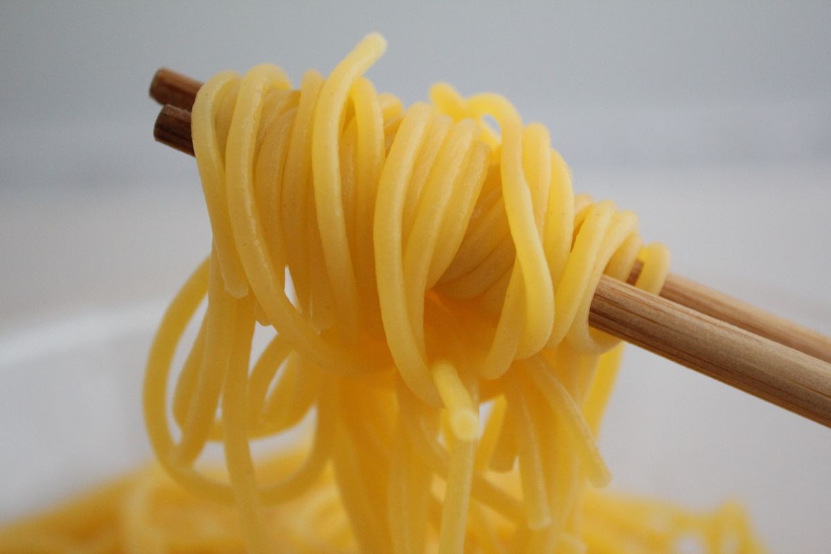 Close-up of yellow noodles wrapped around chopsticks in a minimalistic setting.