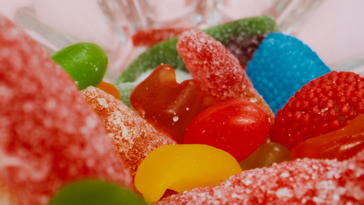 Colorful assortment of gummy and sugary candies in clear glass bowl.