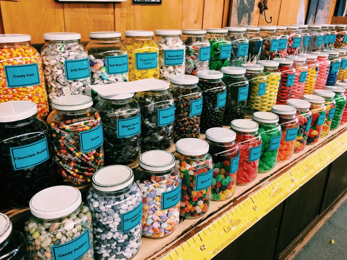 Colorful jars of assorted candies neatly arranged on a store shelf for sale.
