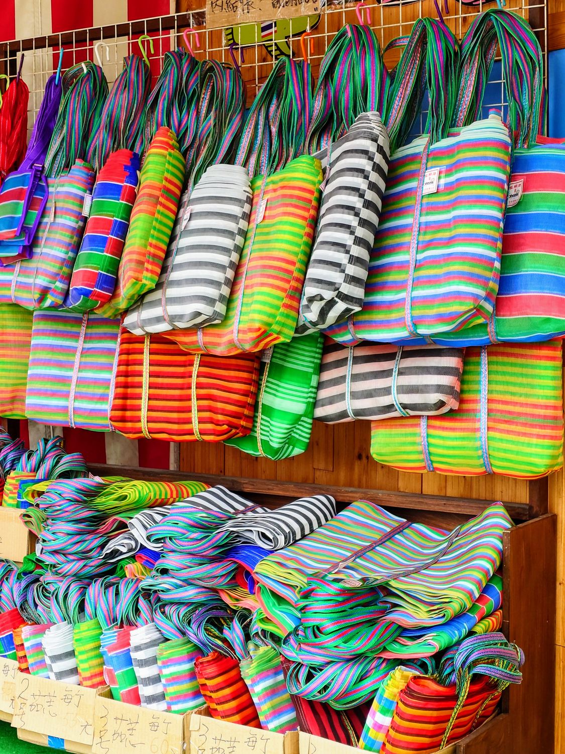 Colorful striped bags and mats displayed at an outdoor market stall, perfect for shopping enthusiasts.