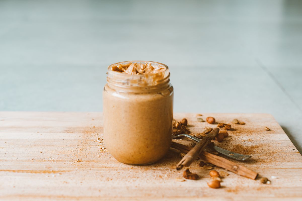Creamy homemade peanut butter in a jar with cinnamon sticks on a wooden board.