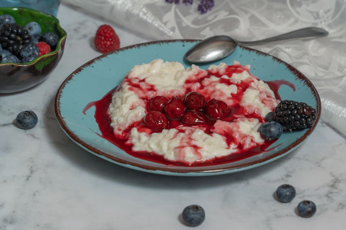 Creamy rice porridge topped with fresh berries and cherry sauce, perfect for breakfast or dessert.