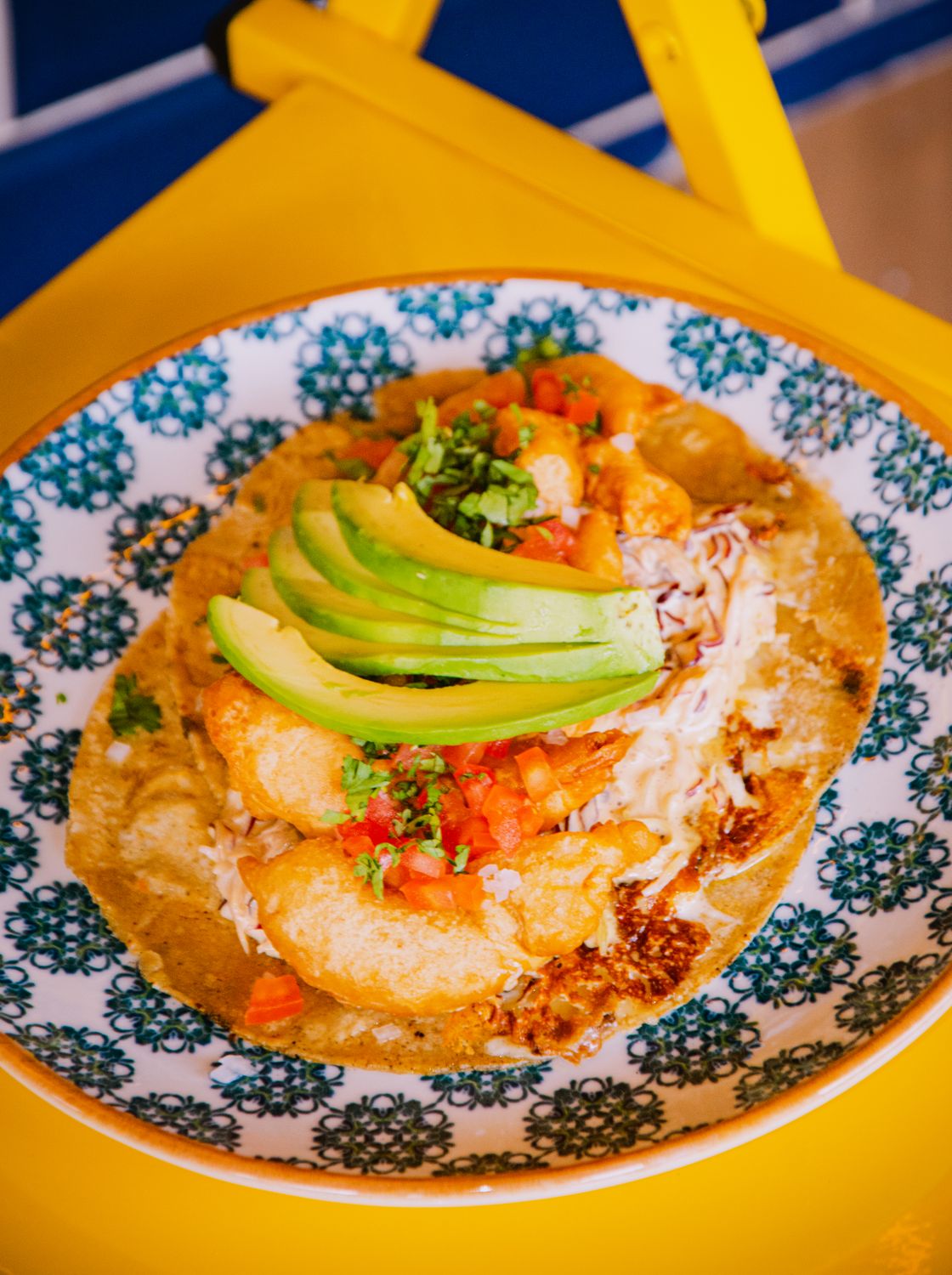 Crisp Baja fish taco topped with fresh avocado slices on a decorative plate.