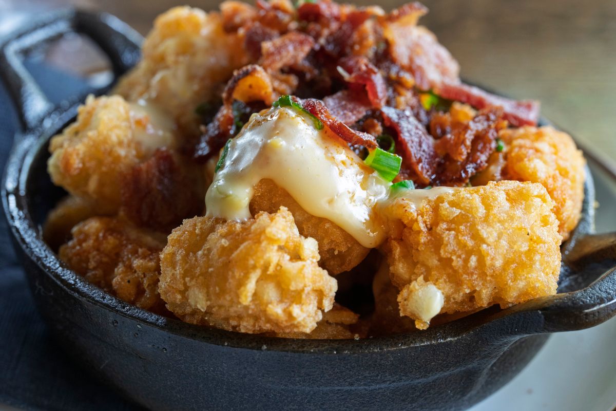 Crispy tater tots topped with melted cheese and bacon in a skillet.