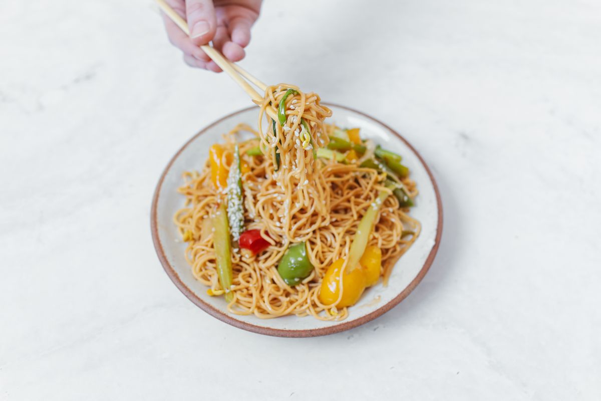 Delicious Asian noodles with colorful vegetables and chopsticks on a bright table.