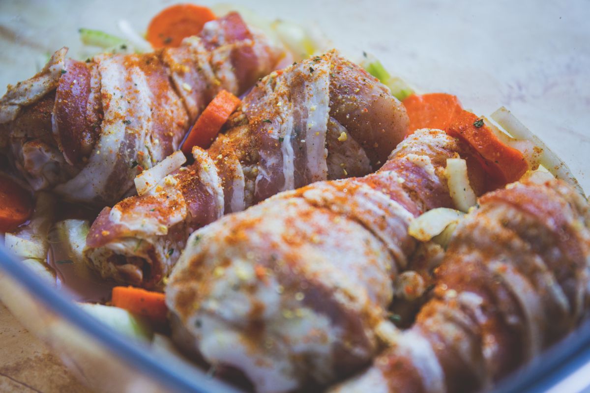 Delicious bacon-wrapped chicken drumsticks seasoned with spices, ready for cooking with vegetables.