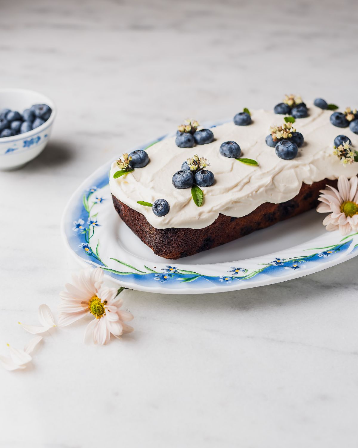 Delicious blueberry cake topped with cream frosting and flowers, set on a floral plate.