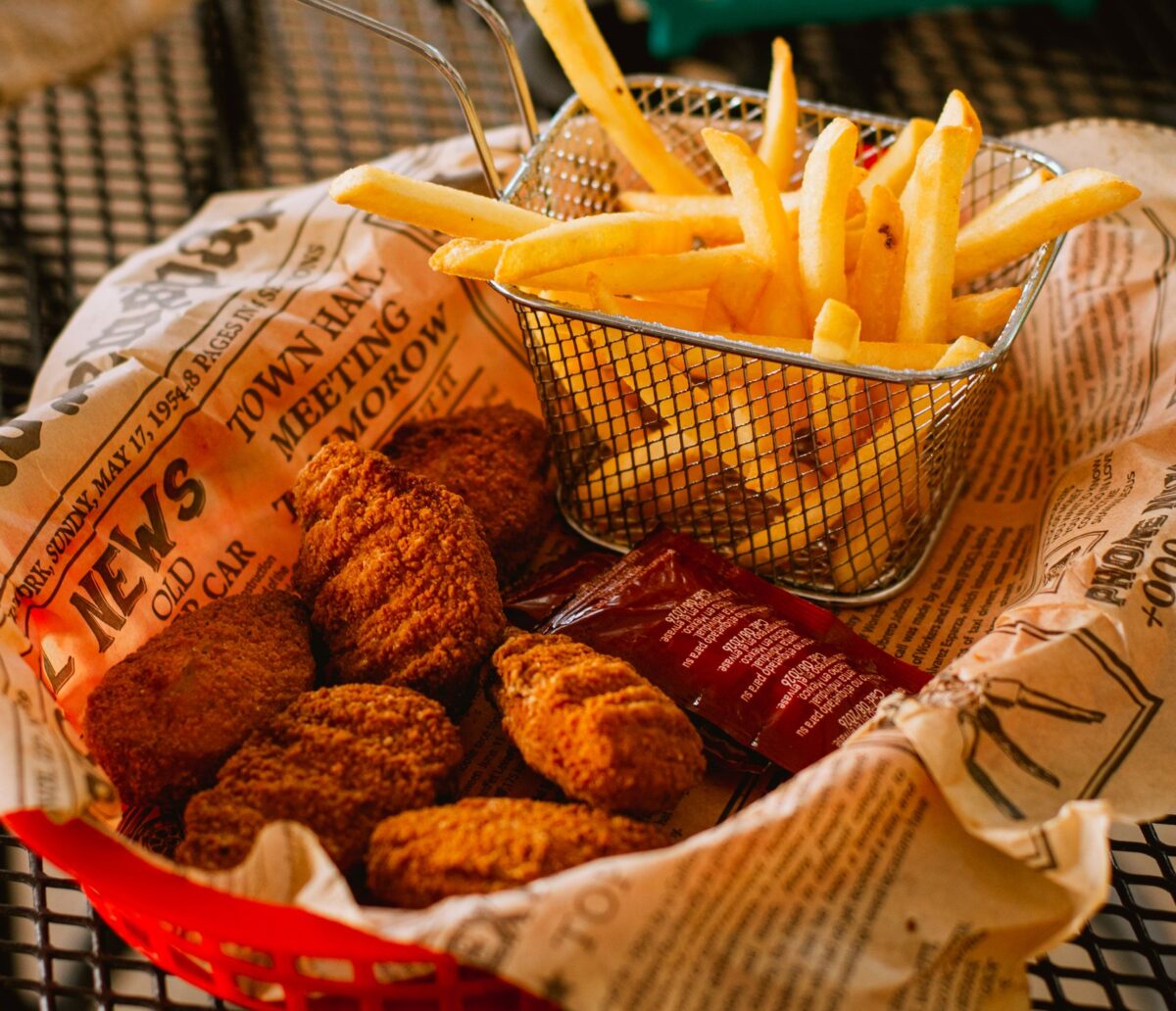 Delicious crispy chicken nuggets and golden fries served in a basket with ketchup on a rustic table.