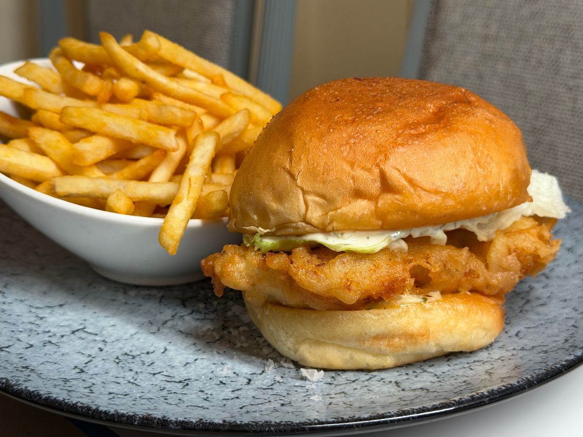 Delicious crispy fish sandwich served with a side of golden French fries on a stylish plate for a perfect meal.