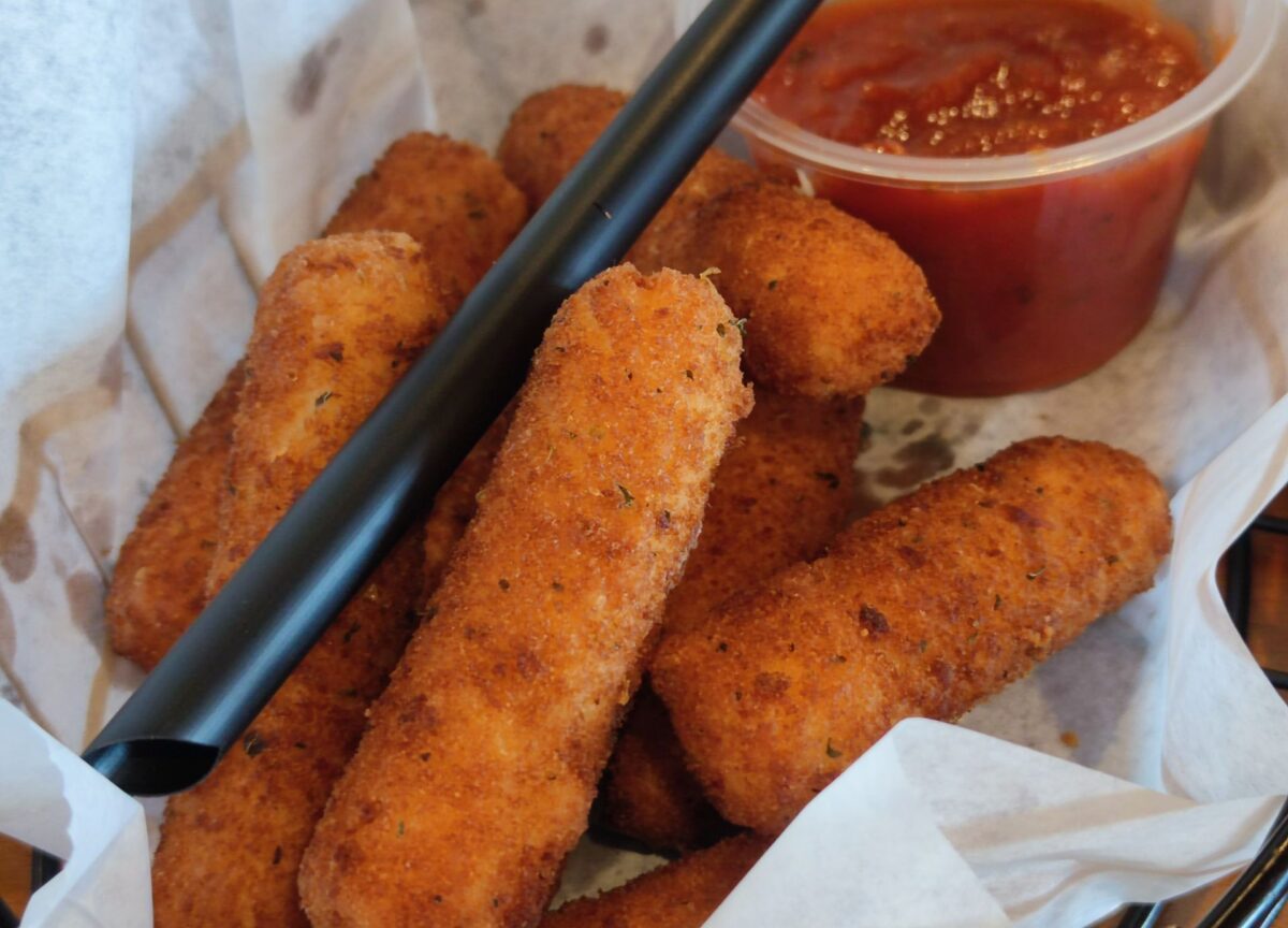 Delicious crispy mozzarella sticks with marinara sauce served in a basket, perfect for a snack or appetizer.