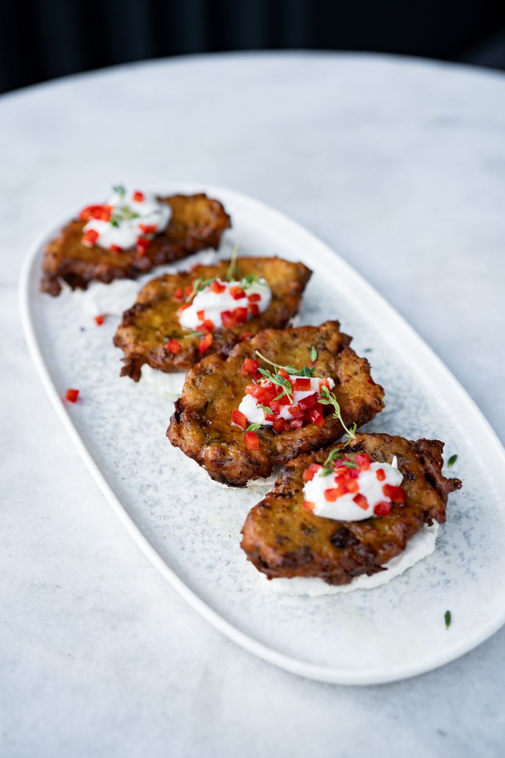 Delicious fried fritters topped with yogurt sauce and herbs served on a white plate.