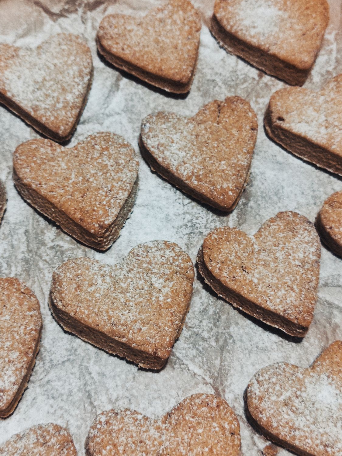 Delicious heart-shaped cookies sprinkled with powdered sugar on baking paper.