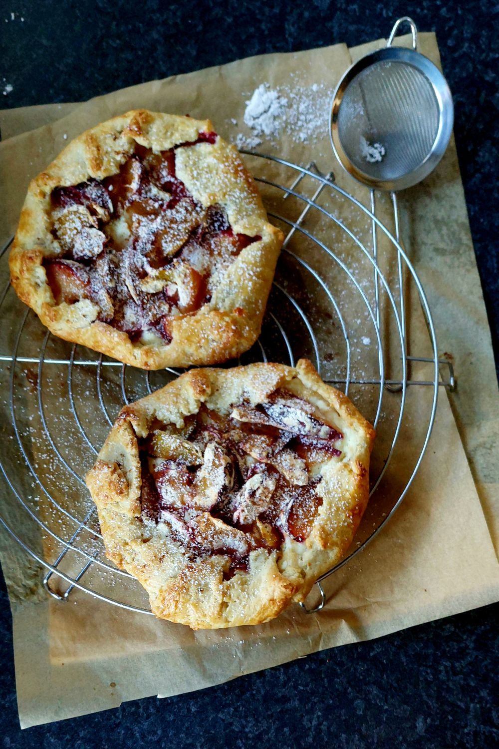 Forget Perfect Pie Crust, This Rustic Plum Galette Makes Messy Look Delicious 1 Delicious homemade fruit galettes with powdered sugar on a cooling rack.