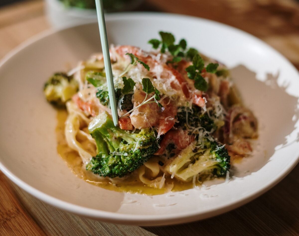 5 Delicious Dishes You Can Make With Broccoli 1 Delicious Italian pasta dish being garnished by hand, showcasing fresh ingredients.