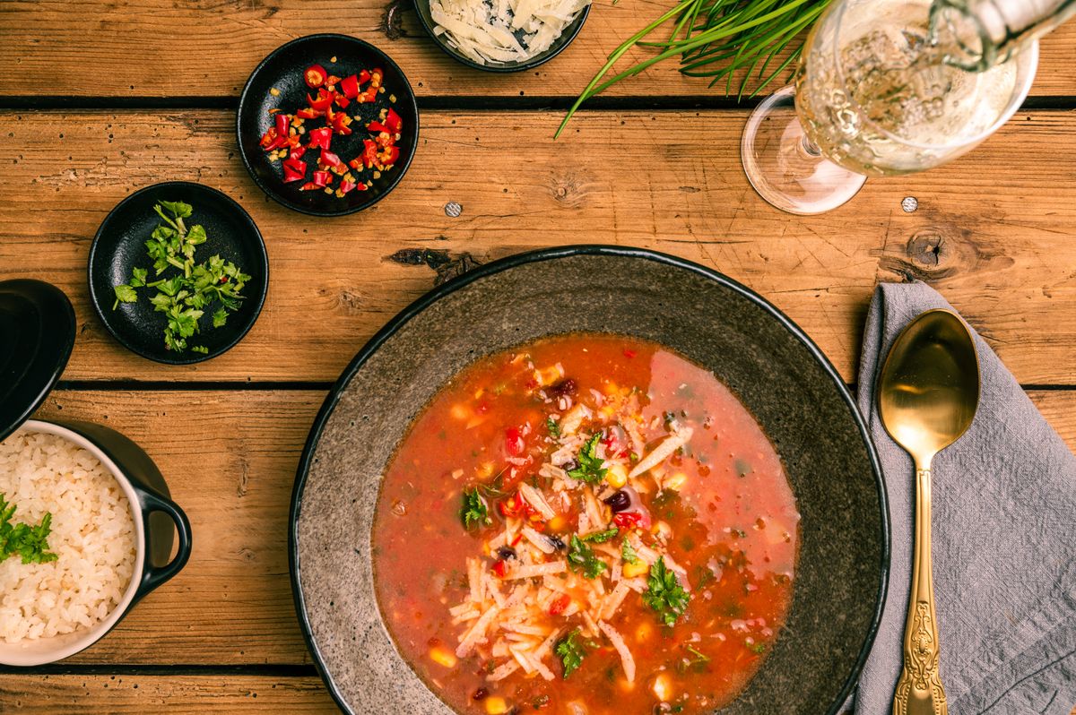 Delicious Mexican soup with rice, chili peppers, and fresh herbs, elegantly presented on a rustic wooden table.