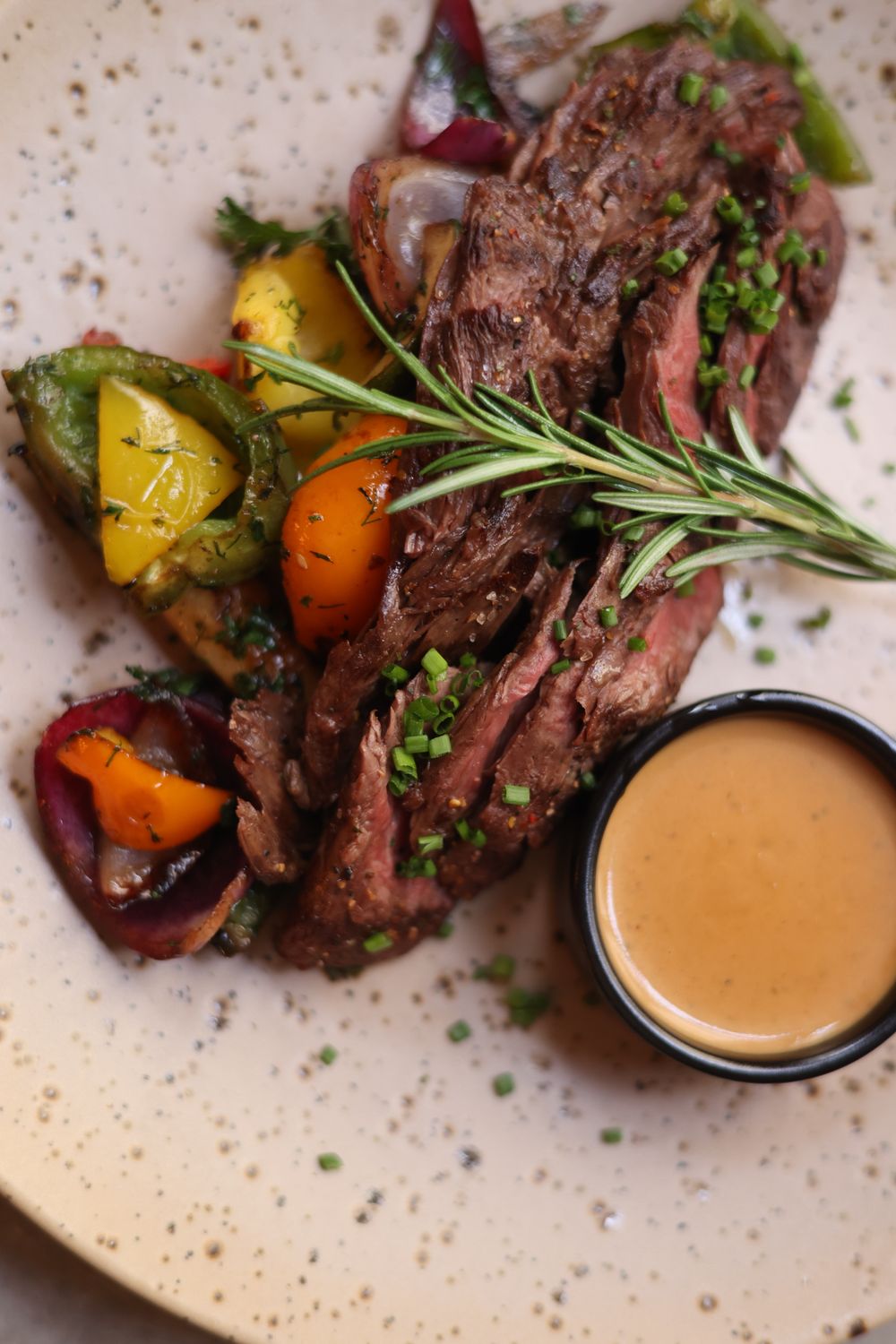 Delicious roasted lamb topped with chives beside grilled vegetables and a serving of gravy.