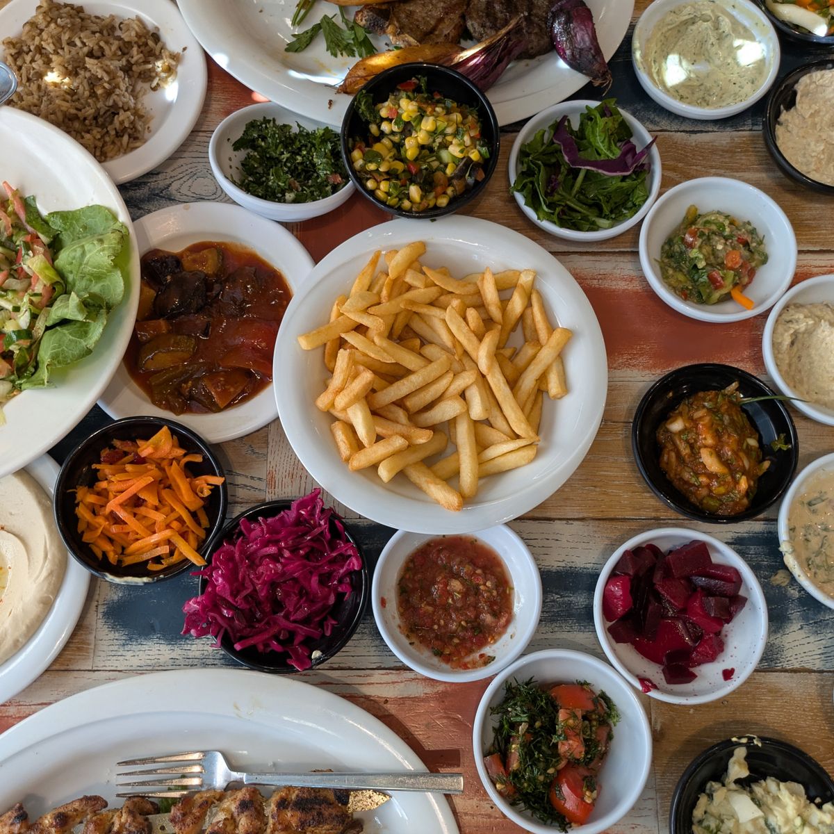 Delicious spread of Middle Eastern mezze with fries, salads, and dips on a wooden table.
