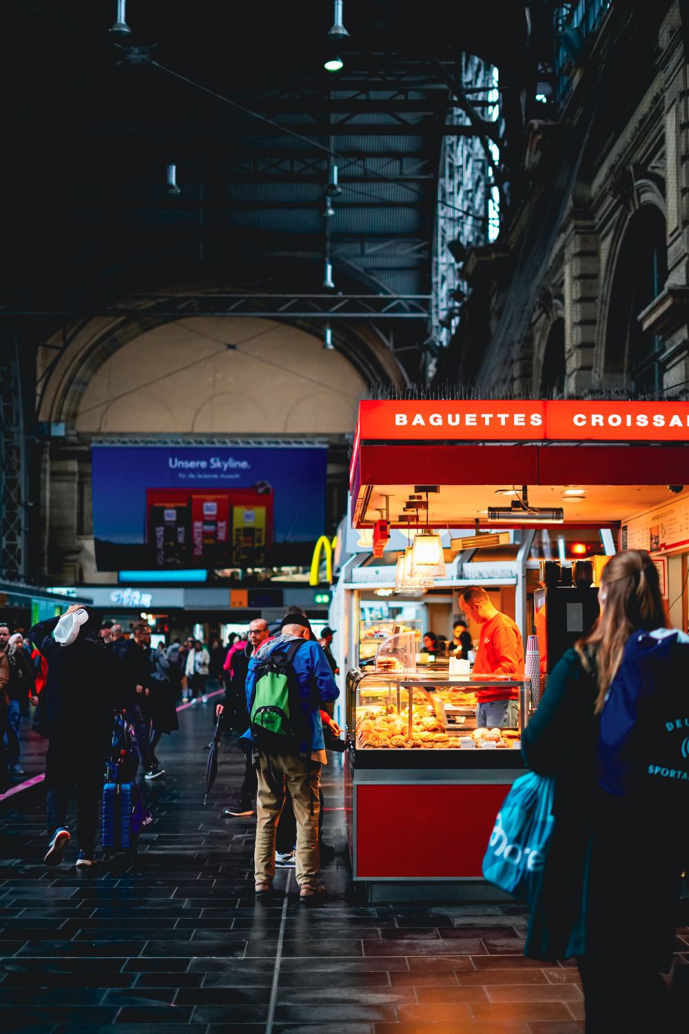 Frankfurt train station with a bakery stand selling baguettes and croissants, bustling with people.