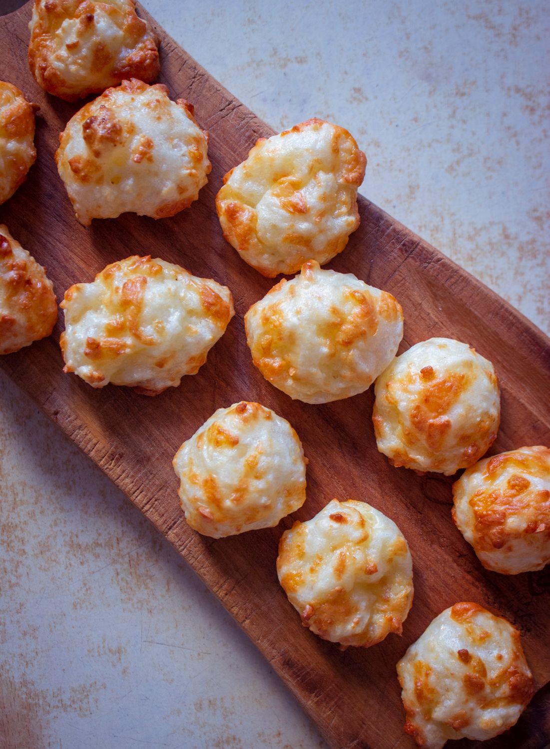 Freshly baked cheese puffs arranged on a rustic wooden board, showcasing a delicious snack option.