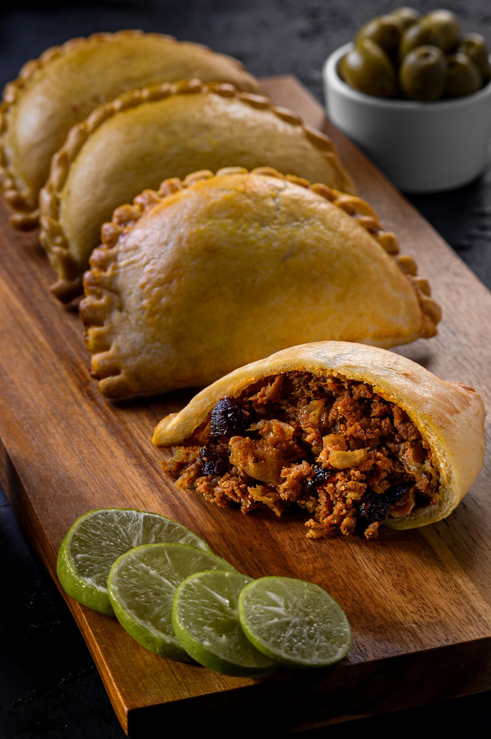 Freshly baked Peruvian empanadas filled with beef, served with lime slices on a wooden board.