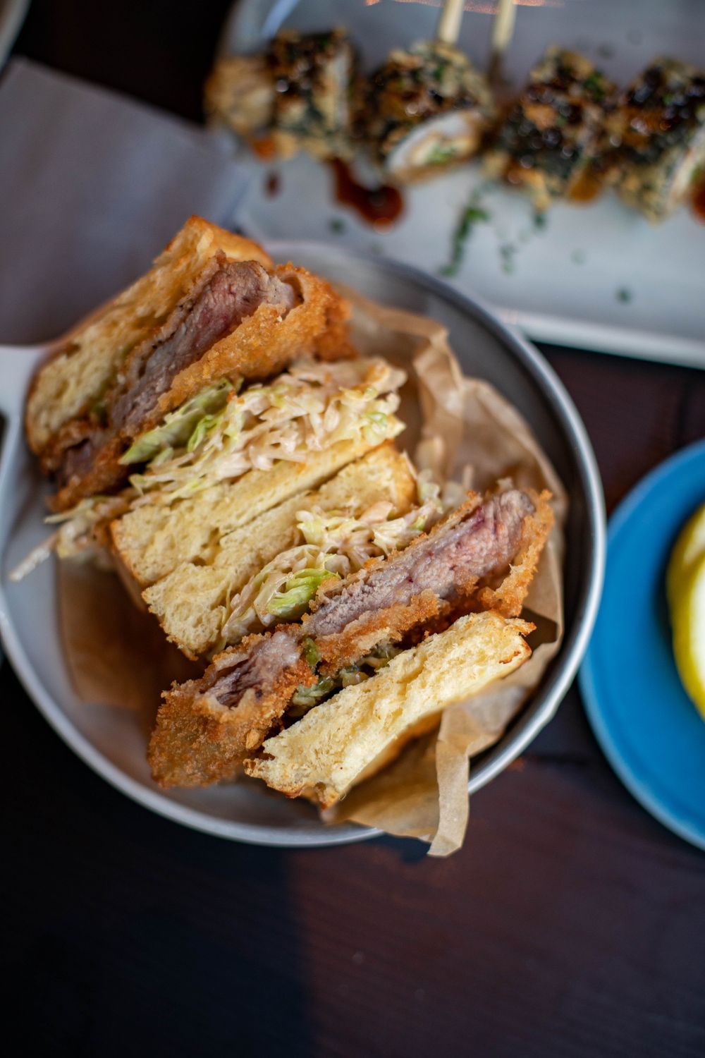 From above of halved sandwich in bowl with set of sushi against blurred background