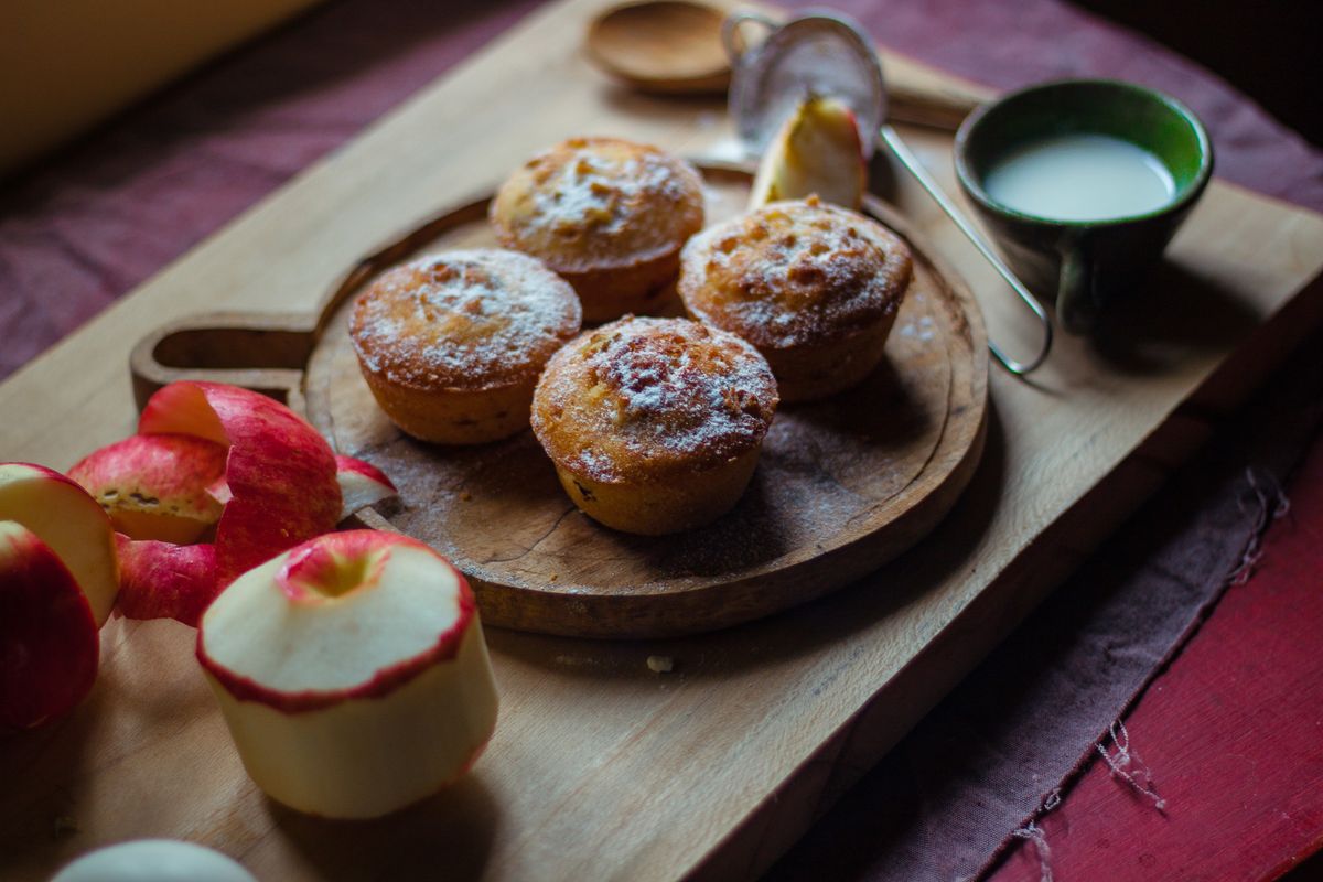 From above of yummy homemade muffins served with unpeeled apples and tea on wooden tray