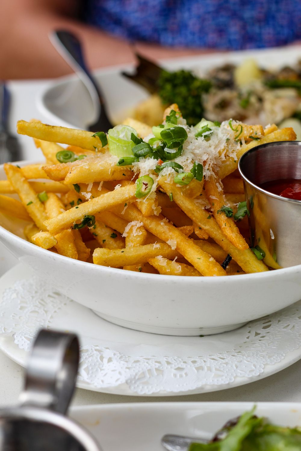 Golden crispy French fries garnished with scallions and Parmesan, accompanied by ketchup in a dining setting.