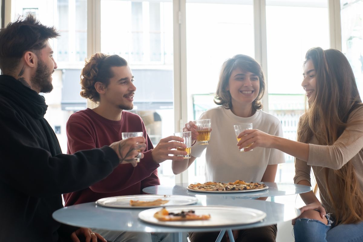 Group of friends sharing pizza and drinks at a table, smiling and enjoying togetherness.