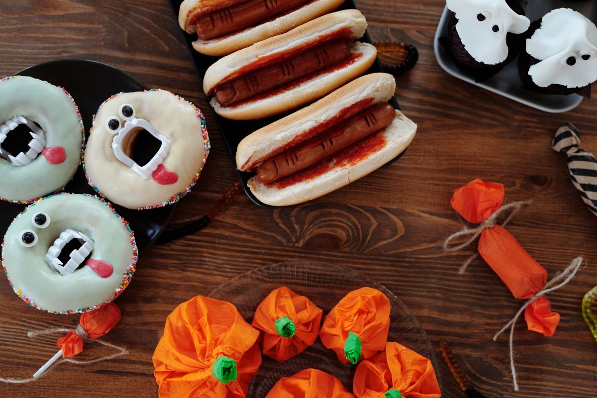 Halloween-themed treats including donuts, hot dogs, and cupcakes styled on a wooden table.