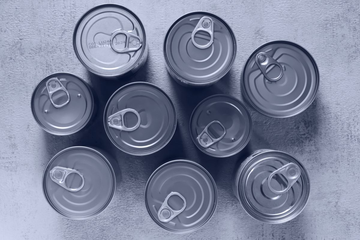 High-angle shot of canned food tins arranged on a rough surface, emphasizing texture and symmetry.