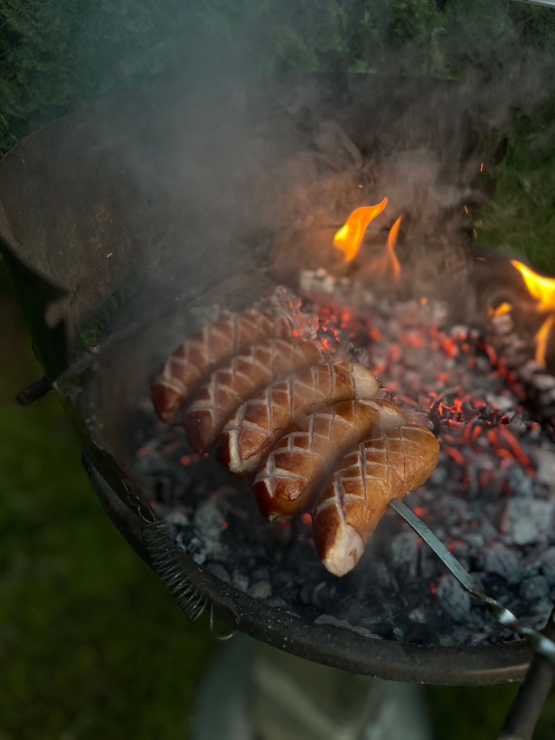 Juicy sausages being grilled over an open flame on a barbecue, perfect for a summer cookout.