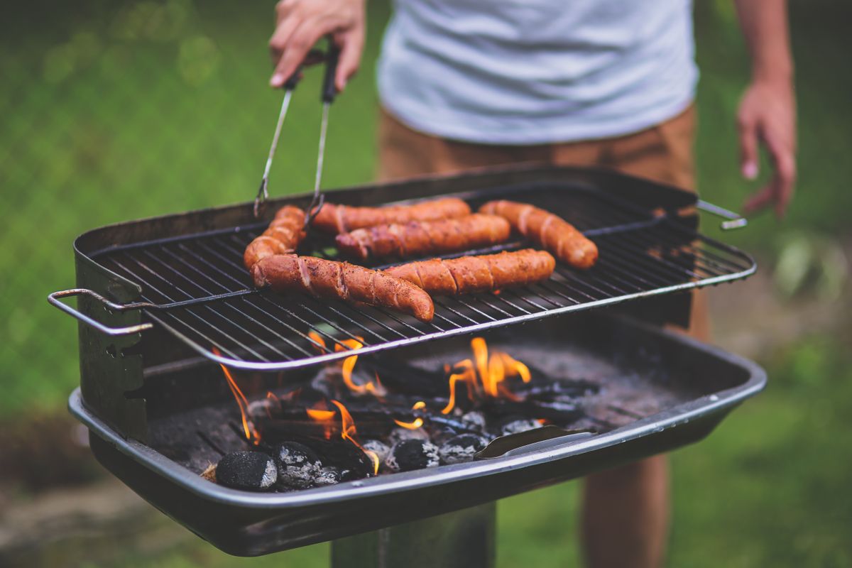 8 Boomer Thanksgiving Traditions Younger Families Are Skipping 1 Man grilling sausages on an outdoor barbecue with flames and charcoal.