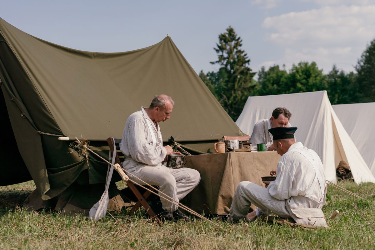 Men in vintage military uniforms at a reenactment camp during summer.
