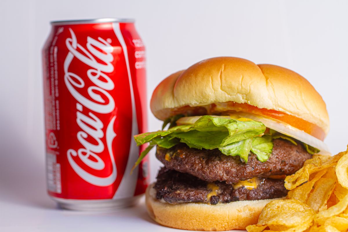 Mouth-watering burger served with a soda can and side of crispy chips.