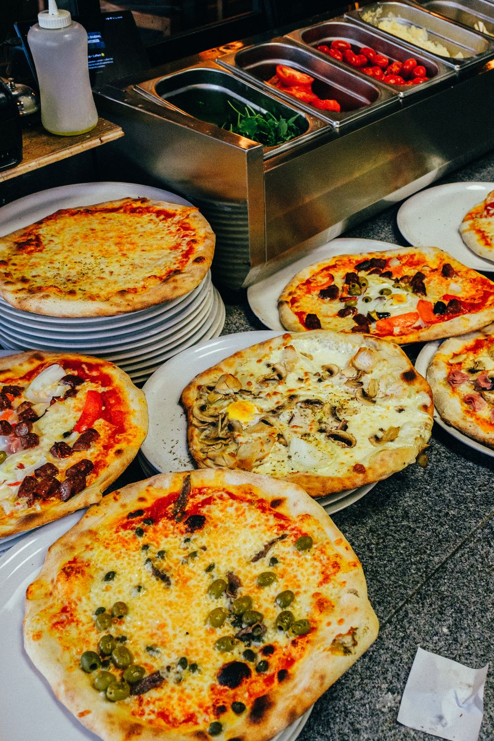Think You Know Pizza? These 9 Regional Styles Might Start a Delicious Argument 1 Multiple freshly baked pizzas displayed in a restaurant setting, showcasing assorted toppings.