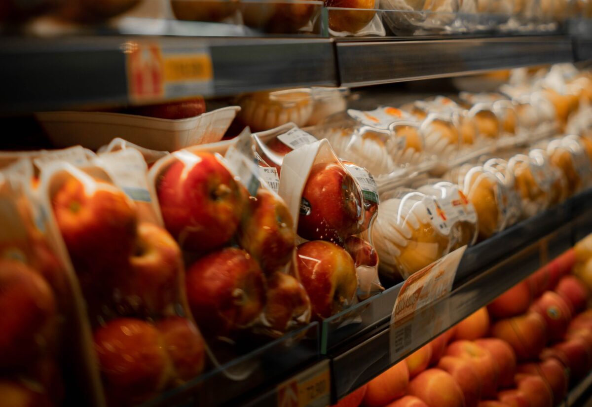 Packaged fresh apples displayed on a supermarket shelf with bright lighting.