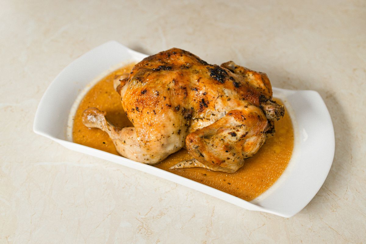 Perfectly roasted chicken on a white plate with savory gravy, ideal for food enthusiasts.